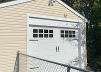 a white garage with a white door and a chain link fence